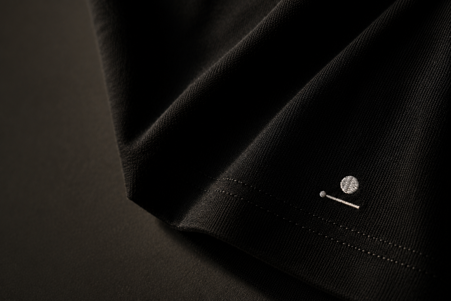Macro detail of a black cotton garment with a subtle embroidered OREN mark.